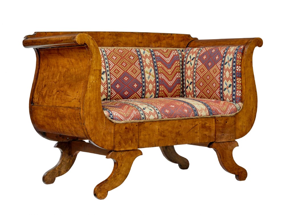 A 19th-century Swedish Empire sofa crafted from golden birch with scrolled ends and splayed legs, featuring geometric pattern textile upholstery.