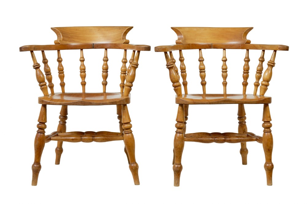 A pair of 19th-century light brown elm elbow chairs featuring curved crest rails, turned spindle backs, shaped saddle seats, and turned legs.