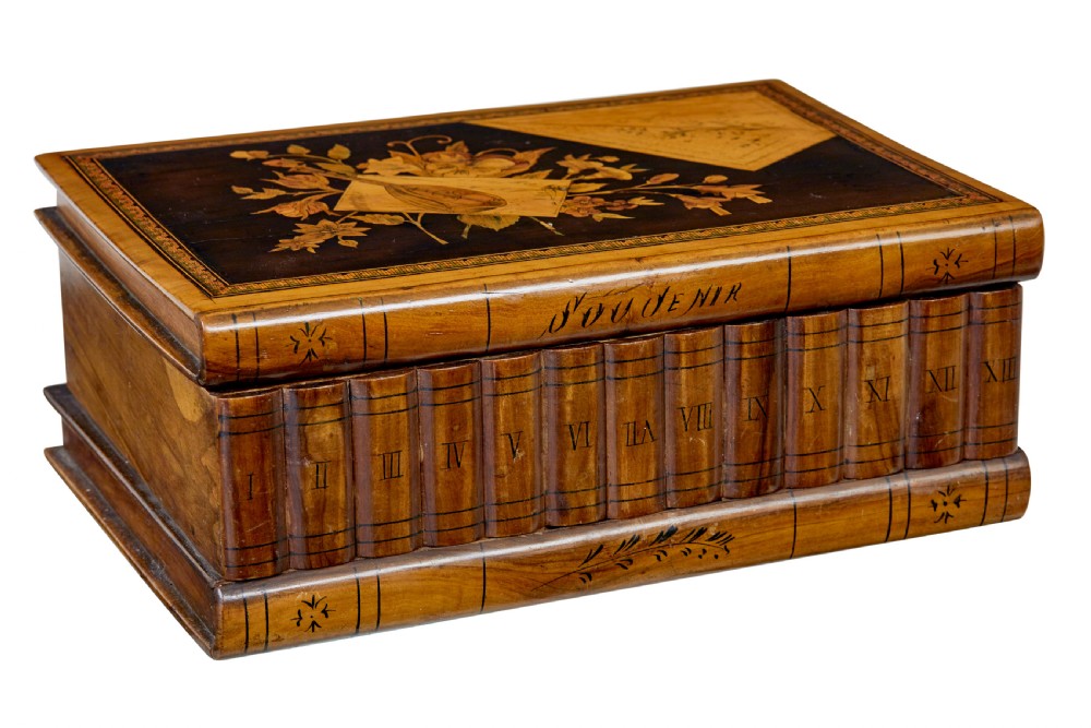 A 19th-century olive wood box crafted in the shape of a stack of books, featuring detailed floral marquetry inlay on the lid and carved book spines on the sides.