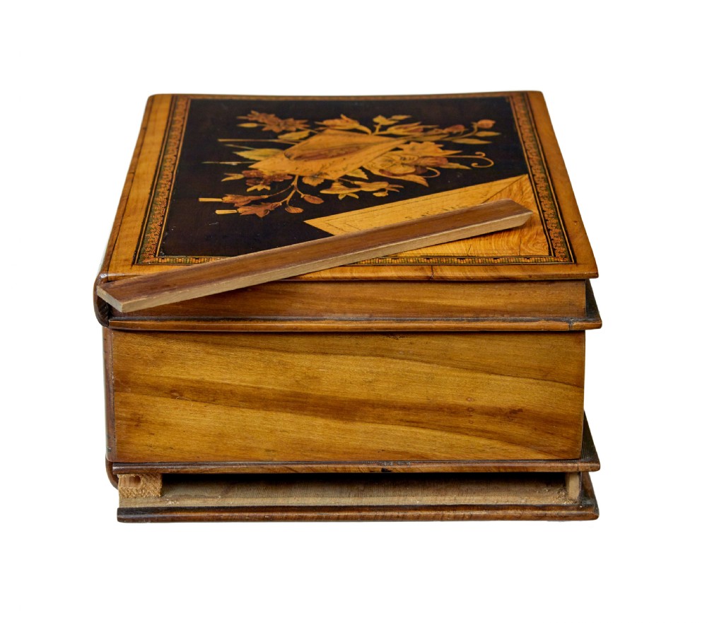 A 19th-century olive wood box crafted in the shape of a stack of books, featuring detailed floral marquetry inlay on the lid and carved book spines on the sides. View V
