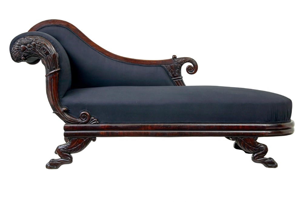 A 19th-century William IV mahogany chaise longue with hand-carved scroll detailing and dark fabric upholstery.