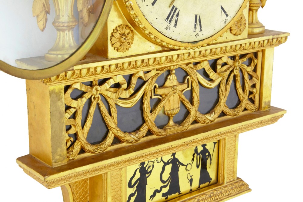 Nineteenth-century Swedish giltwood wall clock adorned with classical silhouettes on eglomise glass panels, carved urns, swags, and twin crested doves. View VI