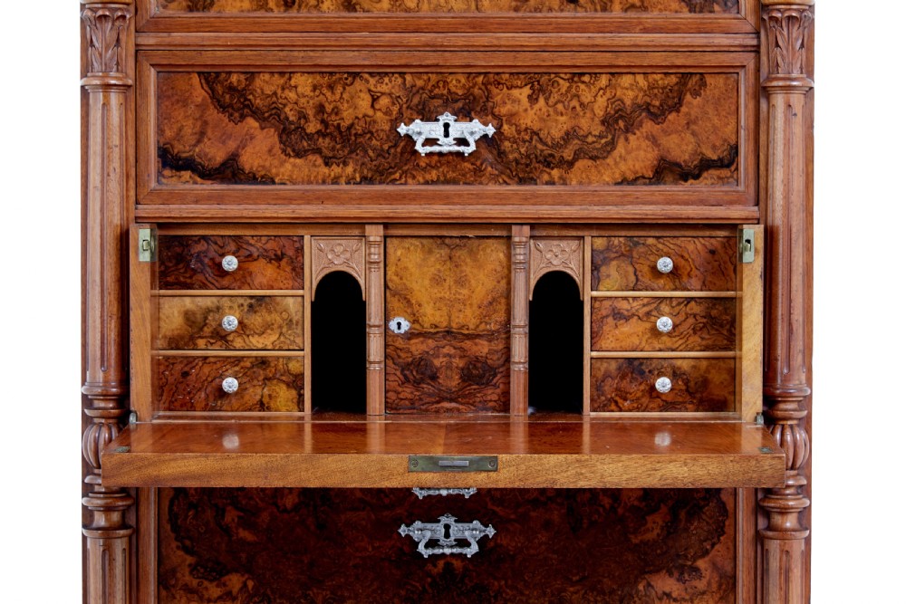 A tall 19th-century burr walnut secretaire chest of drawers featuring bookmatched veneer drawer fronts, fluted side columns, and ornate metal escutcheons. View X