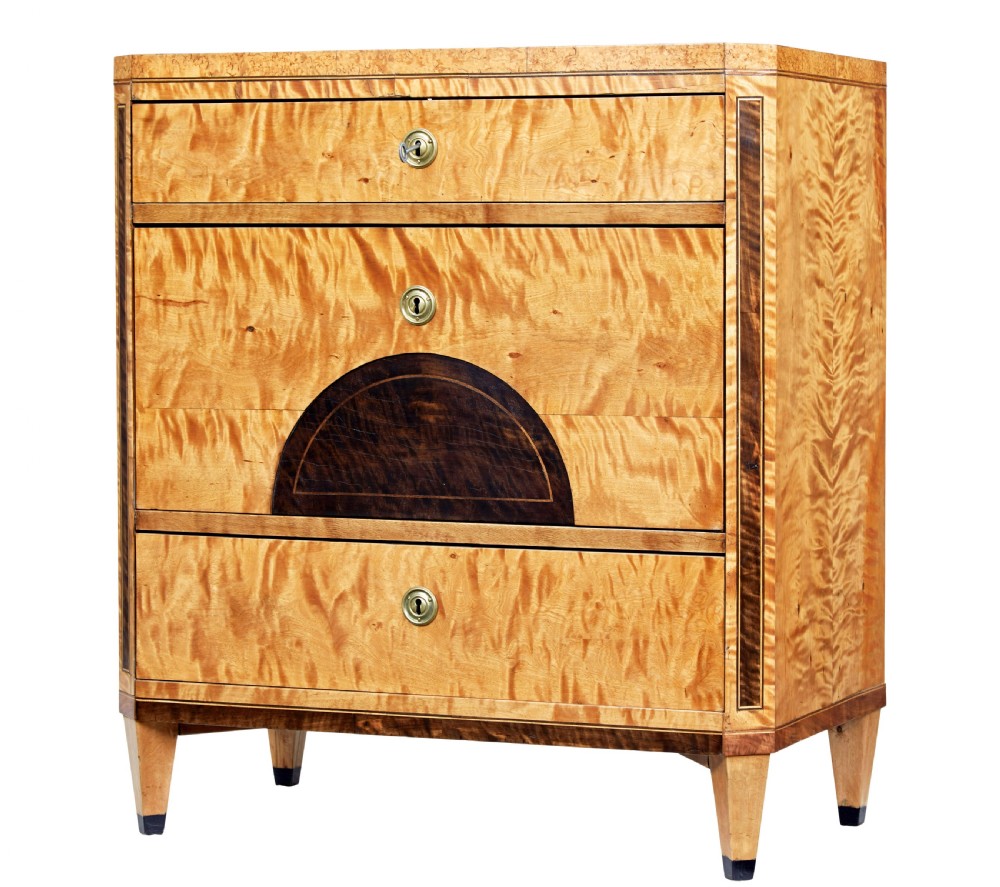 A 19th-century Swedish birch chest of drawers featuring three drawers, flame grain veneers, dark timber inlay, and brass keyhole escutcheons on tapered legs.