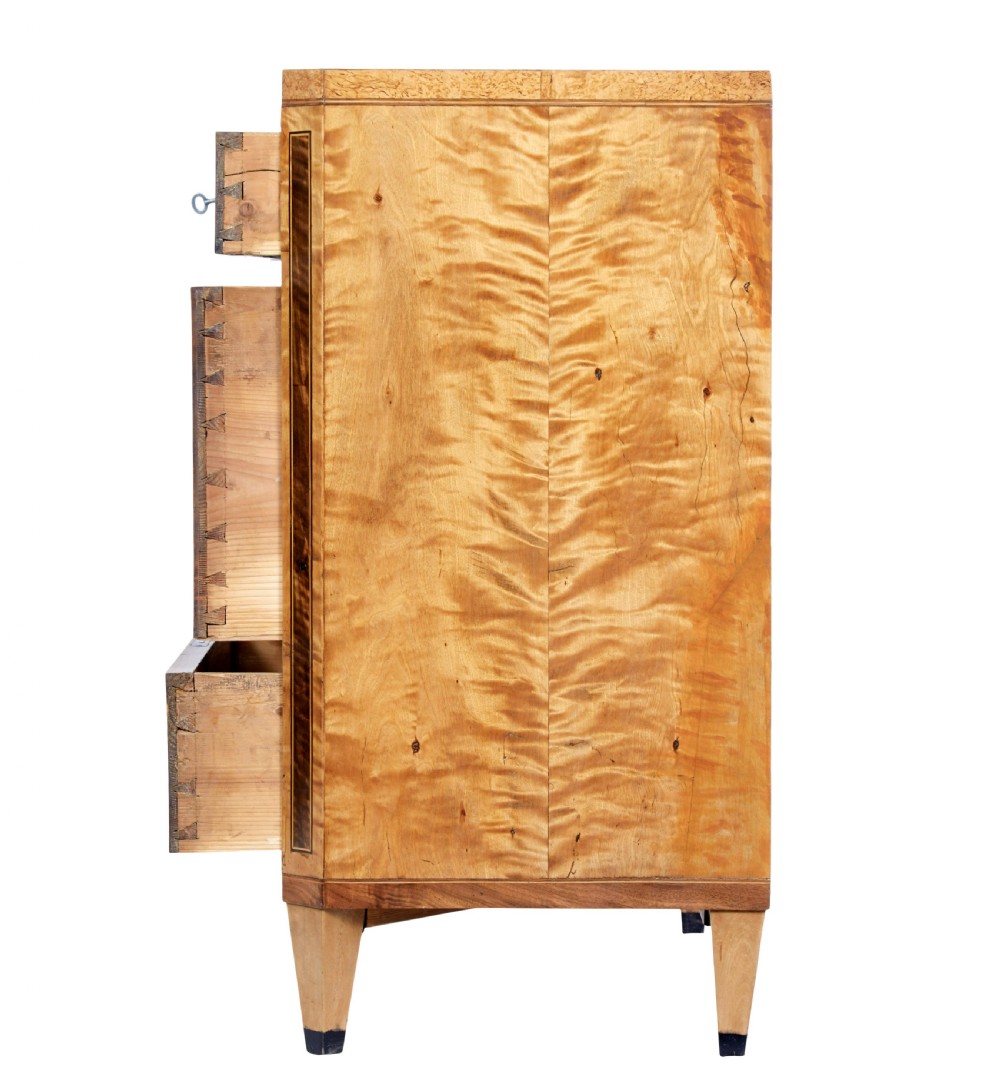 A 19th-century Swedish birch chest of drawers featuring three drawers, flame grain veneers, dark timber inlay, and brass keyhole escutcheons on tapered legs. View II