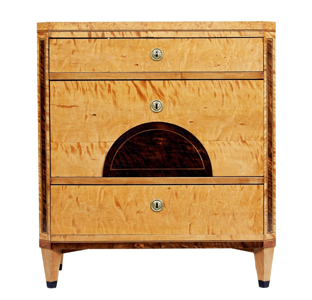 A 19th-century Swedish birch chest of drawers featuring three drawers, flame grain veneers, dark timber inlay, and brass keyhole escutcheons on tapered legs. View V