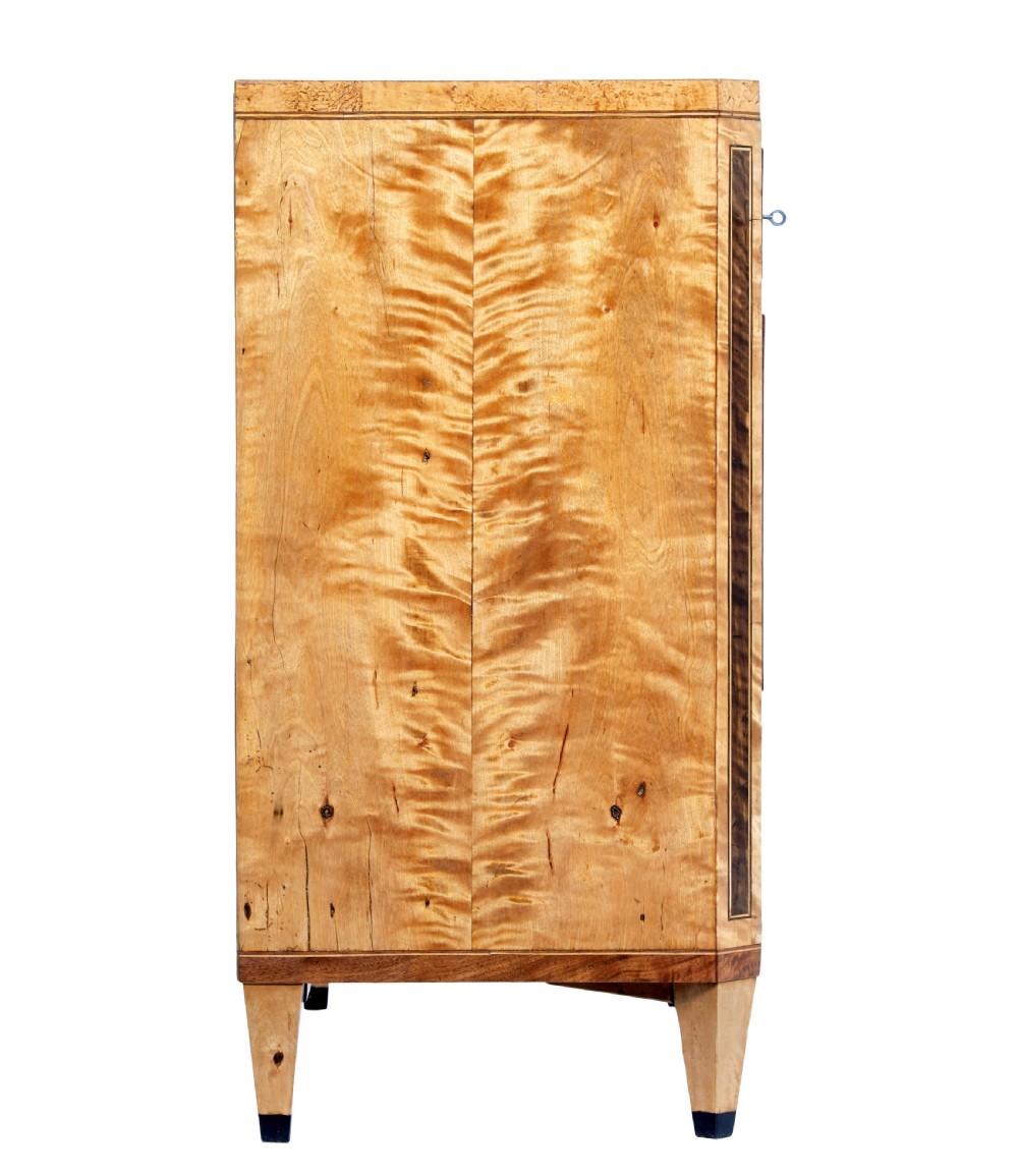 A 19th-century Swedish birch chest of drawers featuring three drawers, flame grain veneers, dark timber inlay, and brass keyhole escutcheons on tapered legs. View VI