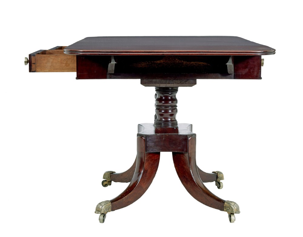 An early Victorian mahogany sofa table featuring two frieze drawers, drop-leaf ends, turned twin column supports, and splayed legs with brass caps and castors. View III