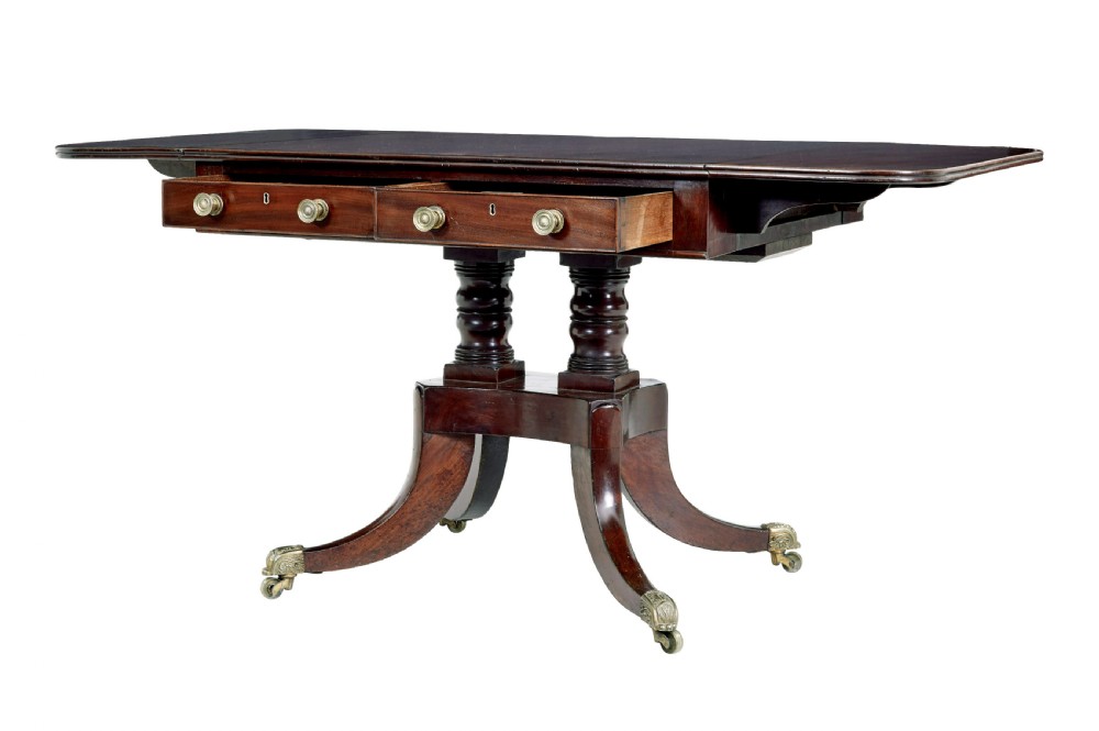 An early Victorian mahogany sofa table featuring two frieze drawers, drop-leaf ends, turned twin column supports, and splayed legs with brass caps and castors. View IV