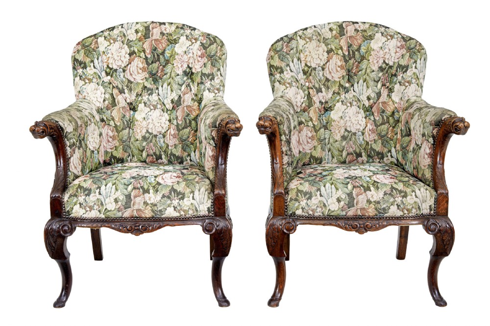 A pair of 19th-century French carved oak armchairs upholstered in a green floral tapestry fabric with carved lion-head armrests.