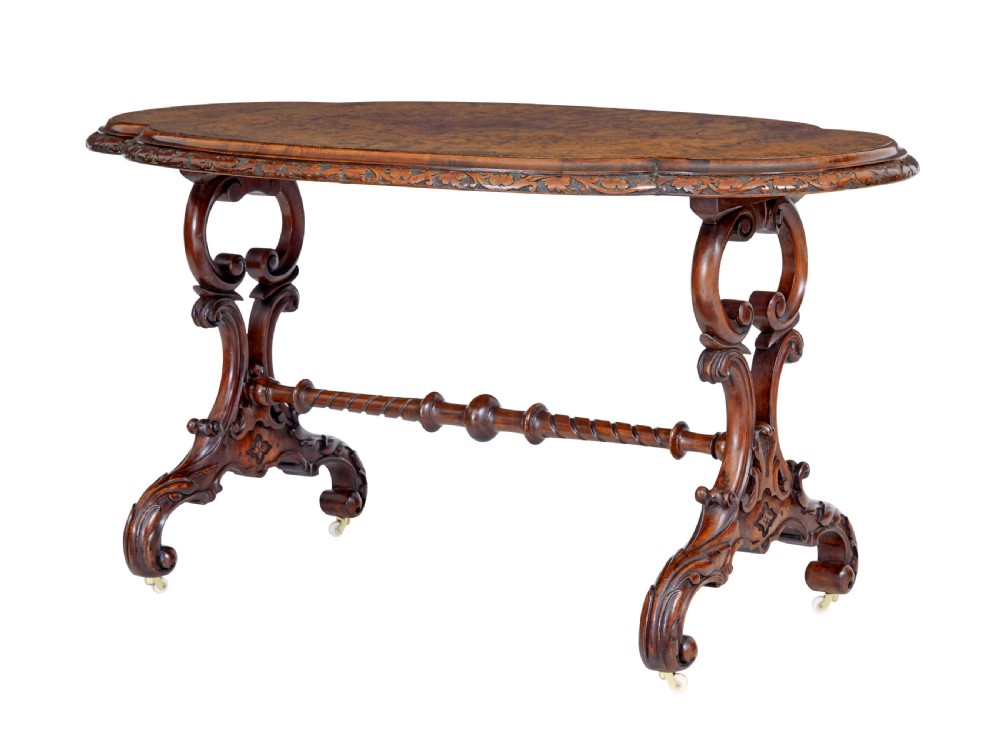 An oval 19th-century Victorian side table crafted from figured burr walnut with carved scroll legs, turned central stretcher, and ceramic castors.