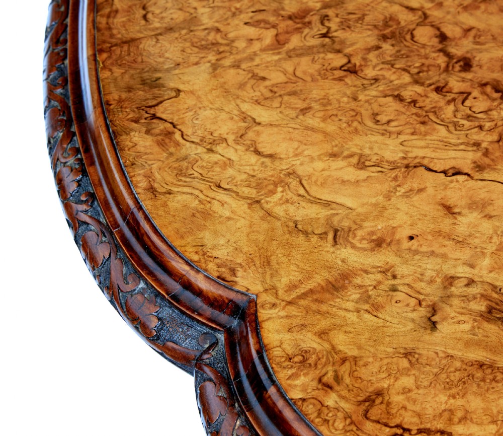 An oval 19th-century Victorian side table crafted from figured burr walnut with carved scroll legs, turned central stretcher, and ceramic castors. View V