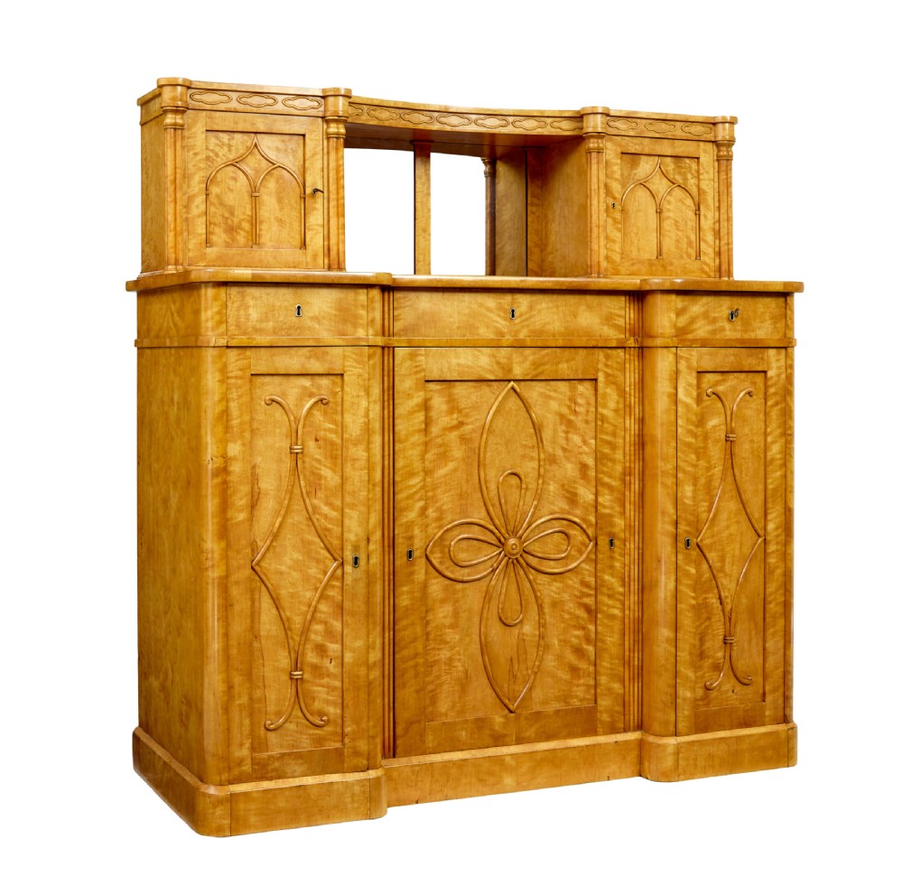 A mid-19th-century Swedish satin birch buffet sideboard featuring a lower three-door cabinet with carved petal applied mouldings and an upper tiered superstructure with Gothic arch cabinet doors.