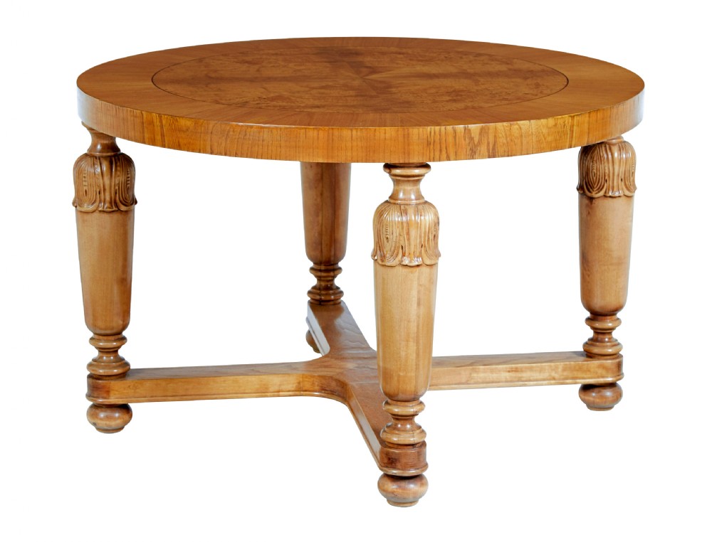 A low circular Art Deco coffee table crafted from light golden birch with an inlaid central panel and carved legs connected by an X-frame stretcher.