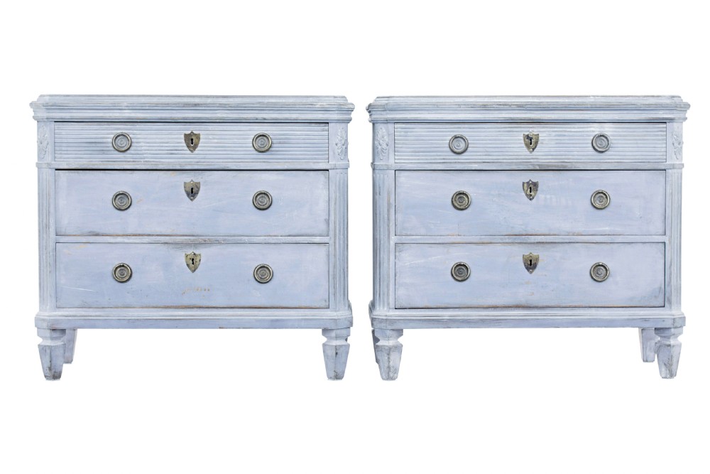 A pair of 19th-century light blue painted Swedish chests of drawers featuring three drawers, fluted sides, circular brass pull handles, and brass shield escutcheons.