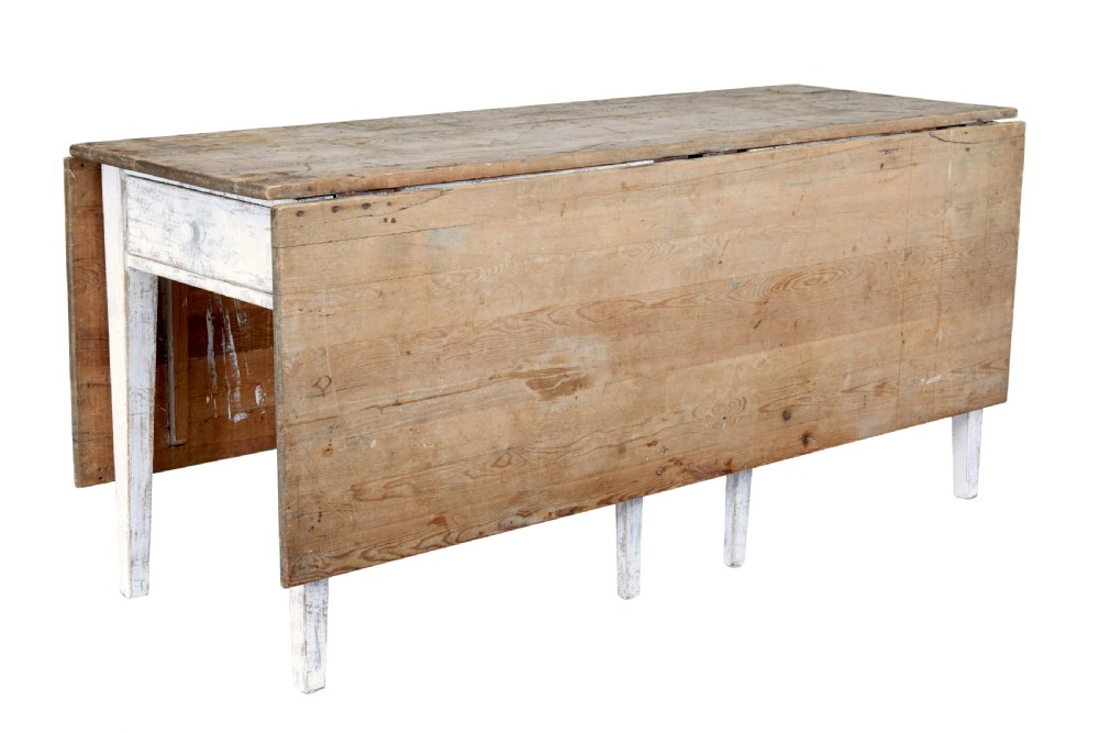 A 19th-century pine drop-leaf kitchen table featuring a natural wood top, hinged side flaps, end drawer, and a white-painted base with tapered square legs.