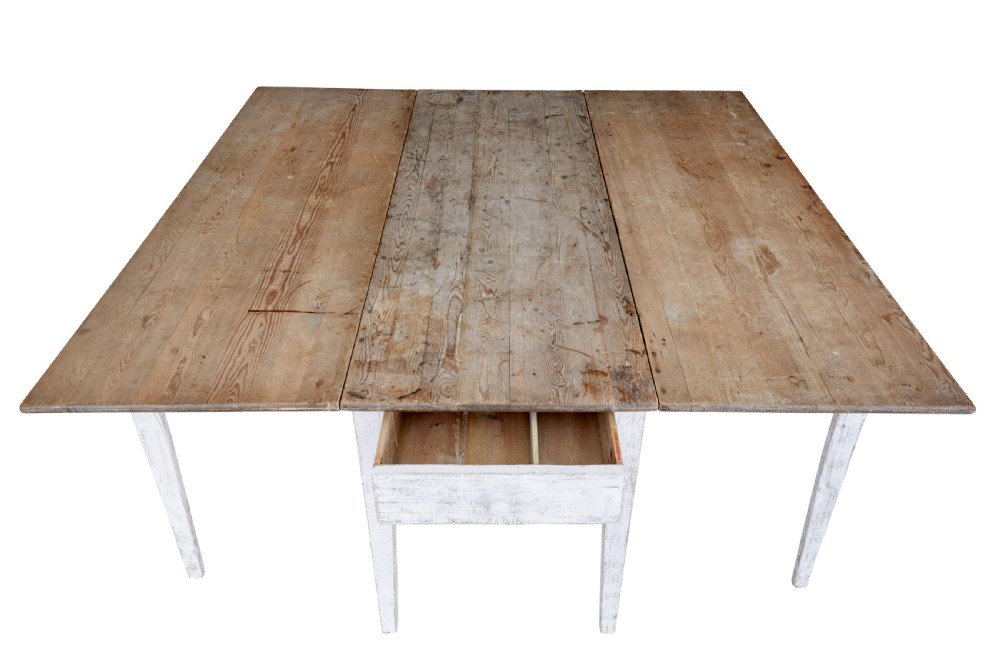 A 19th-century pine drop-leaf kitchen table featuring a natural wood top, hinged side flaps, end drawer, and a white-painted base with tapered square legs. View IX