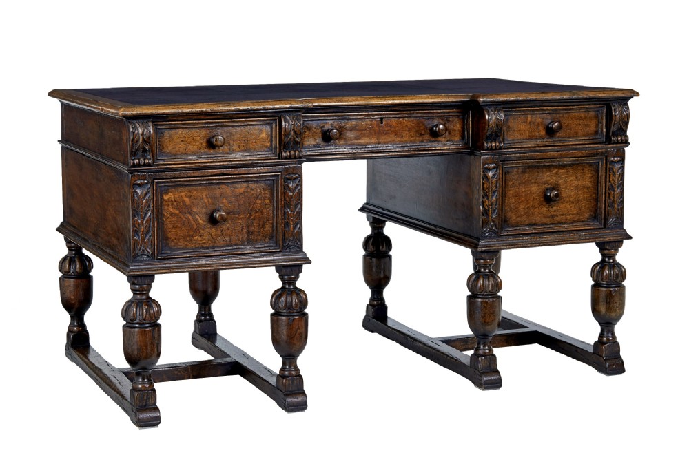 A late nineteenth-century Victorian dark carved oak pedestal desk featuring a leather writing surface, multiple drawers, and turned legs on stretcher bases.