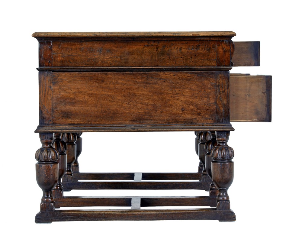A late nineteenth-century Victorian dark carved oak pedestal desk featuring a leather writing surface, multiple drawers, and turned legs on stretcher bases. View V