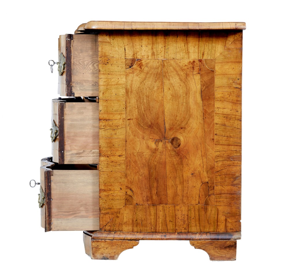 An 18th-century burr walnut serpentine-front chest of drawers featuring three long drawers with ornate brass handles and bracket feet. View V