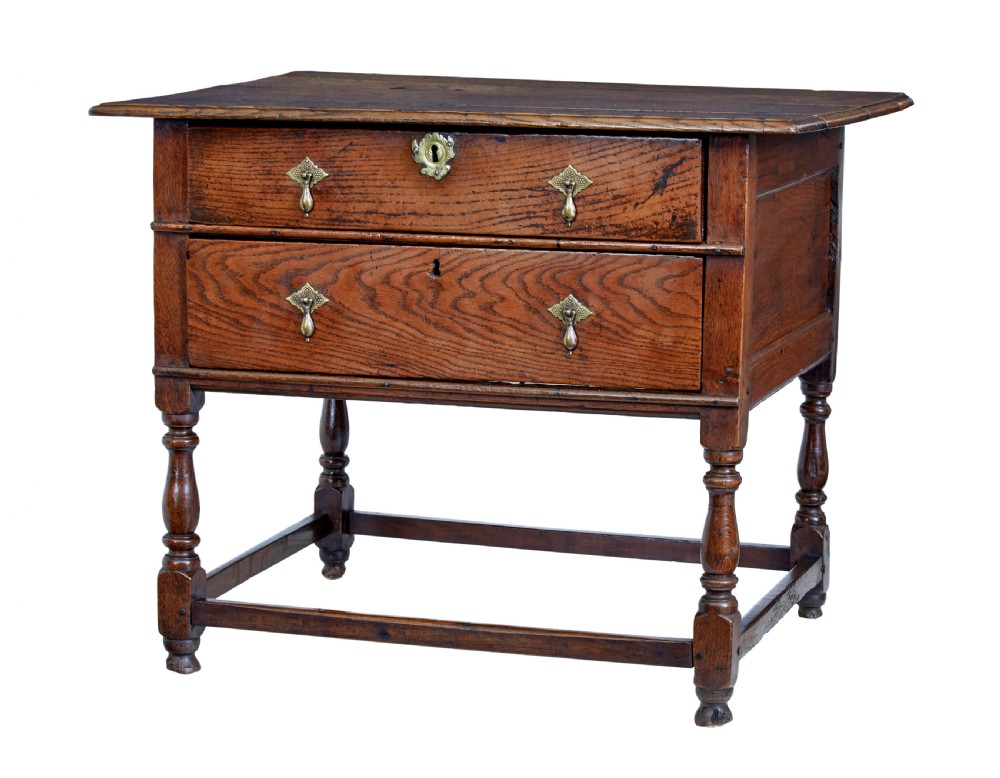 An early 18th-century Georgian oak side table featuring two drawers with brass drop handles, keyhole escutcheons, turned legs, and a box stretcher.