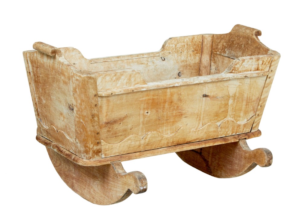 A mid-19th-century Swedish pine rocking cradle with hand-carved handles, scalloped edge detailing, and integrated wooden rockers.
