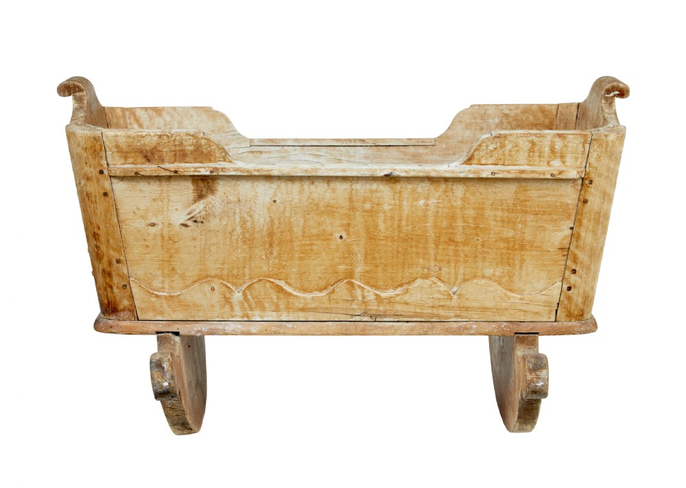 A mid-19th-century Swedish pine rocking cradle with hand-carved handles, scalloped edge detailing, and integrated wooden rockers. View VI