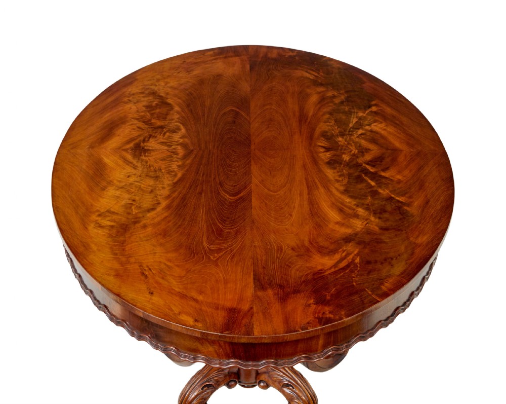 A 19th-century mahogany oval centre table featuring a flame mahogany veneered top, a scalloped apron, and a heavily carved tripod pedestal base with scroll feet. View VII