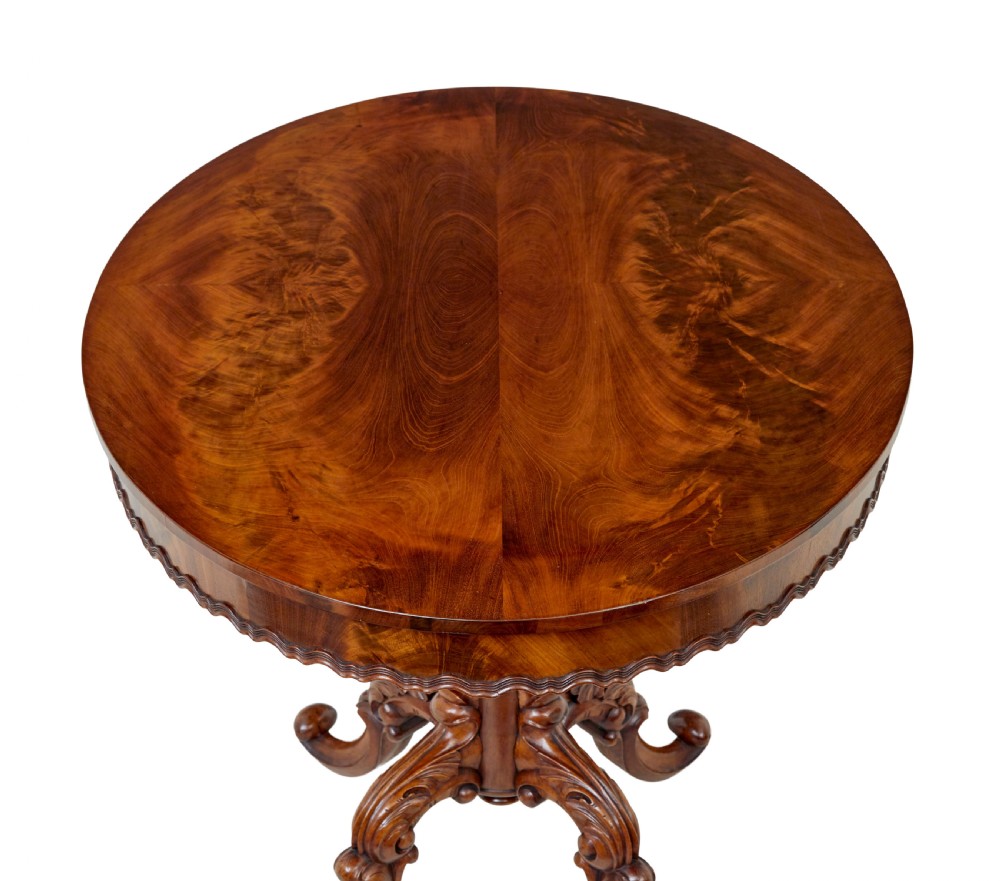 A 19th-century mahogany oval centre table featuring a flame mahogany veneered top, a scalloped apron, and a heavily carved tripod pedestal base with scroll feet. View VIII