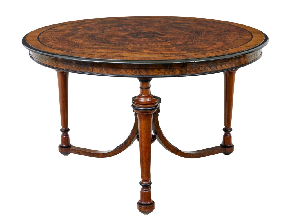 An early 20th-century circular burr walnut occasional table featuring an inlaid top, decorative apron, and three turned legs connected to a central carved triform base. View II