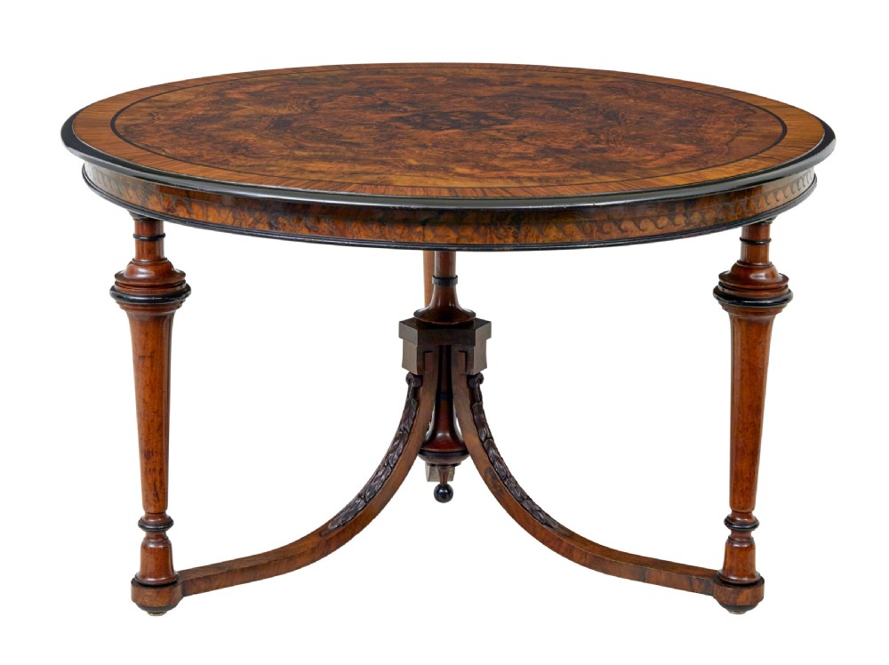 An early 20th-century circular burr walnut occasional table featuring an inlaid top, decorative apron, and three turned legs connected to a central carved triform base. View III