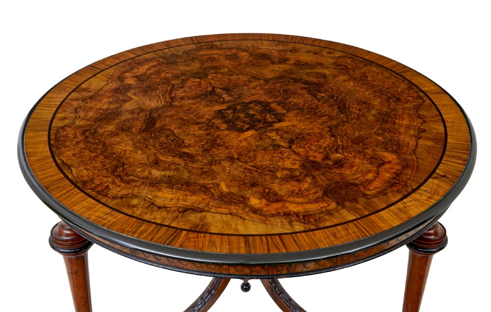 An early 20th-century circular burr walnut occasional table featuring an inlaid top, decorative apron, and three turned legs connected to a central carved triform base. View IV