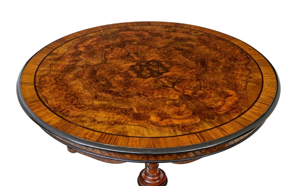 An early 20th-century circular burr walnut occasional table featuring an inlaid top, decorative apron, and three turned legs connected to a central carved triform base. View V