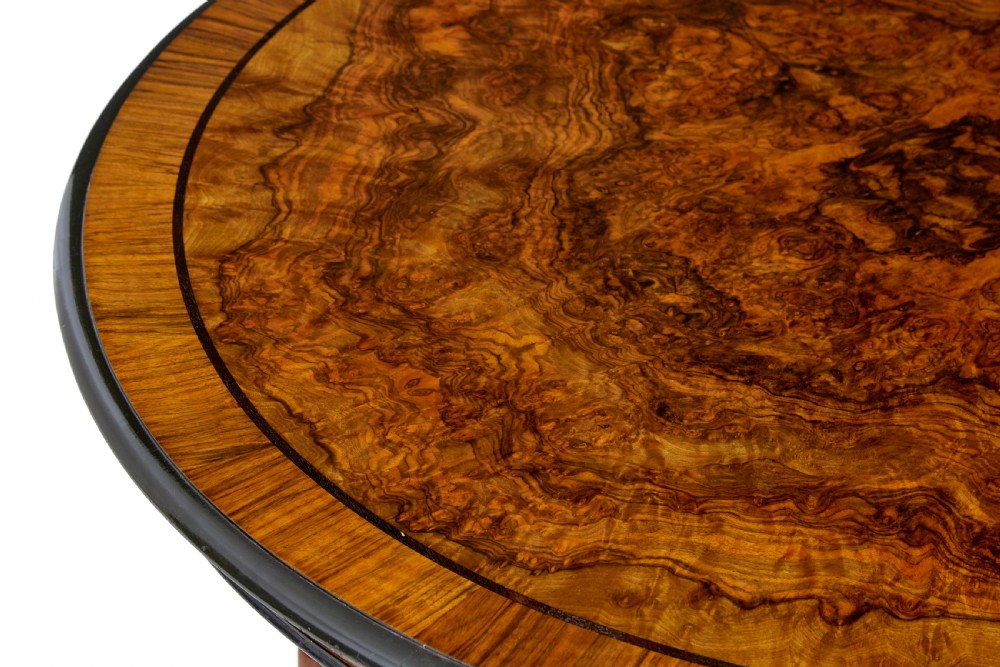 An early 20th-century circular burr walnut occasional table featuring an inlaid top, decorative apron, and three turned legs connected to a central carved triform base. View VI