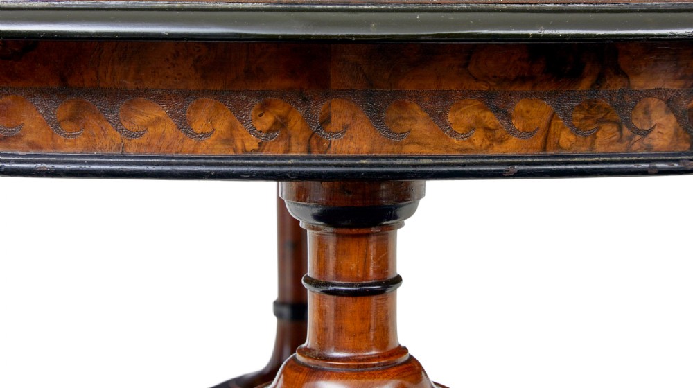 An early 20th-century circular burr walnut occasional table featuring an inlaid top, decorative apron, and three turned legs connected to a central carved triform base. View VII
