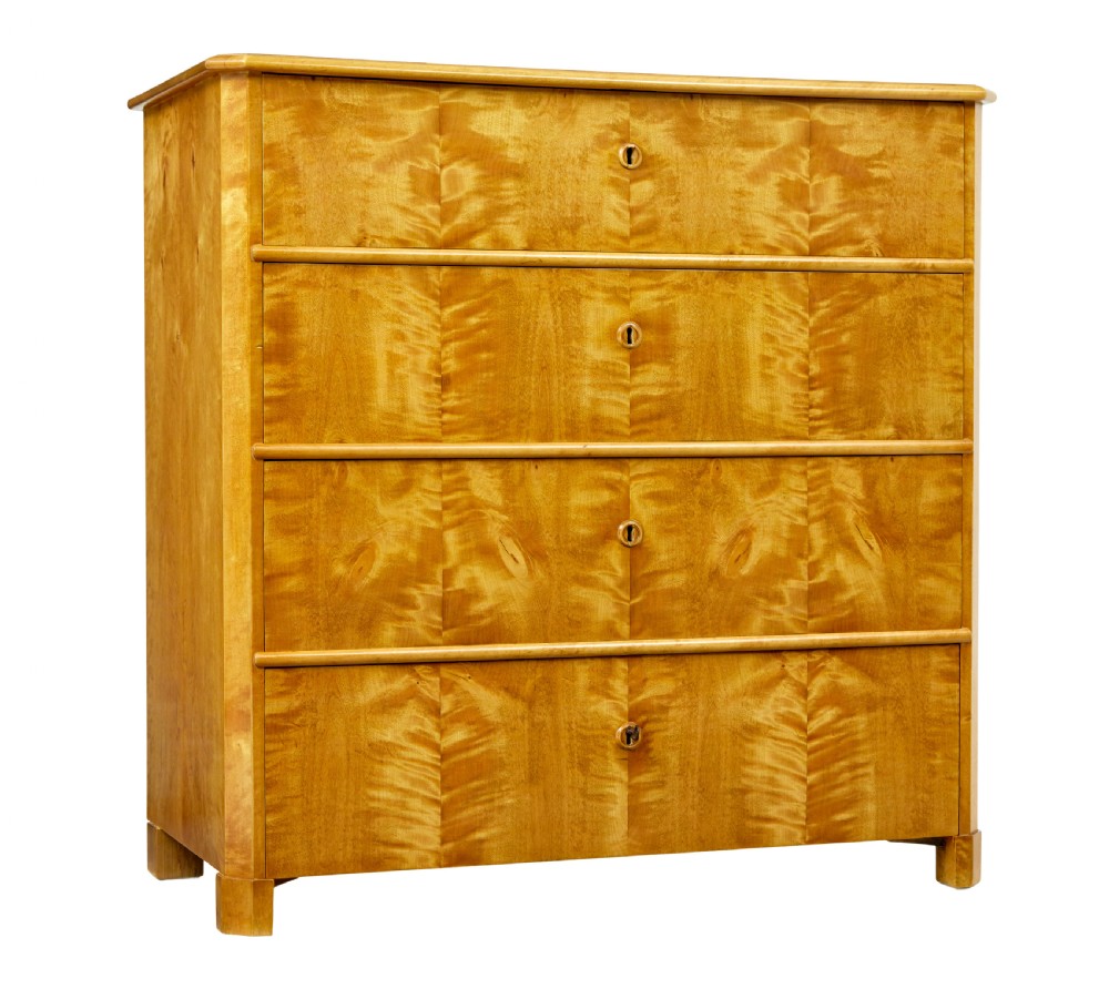 A 19th-century Swedish chest of four drawers crafted from golden flame birch veneer with simple keyhole escutcheons and square legs.