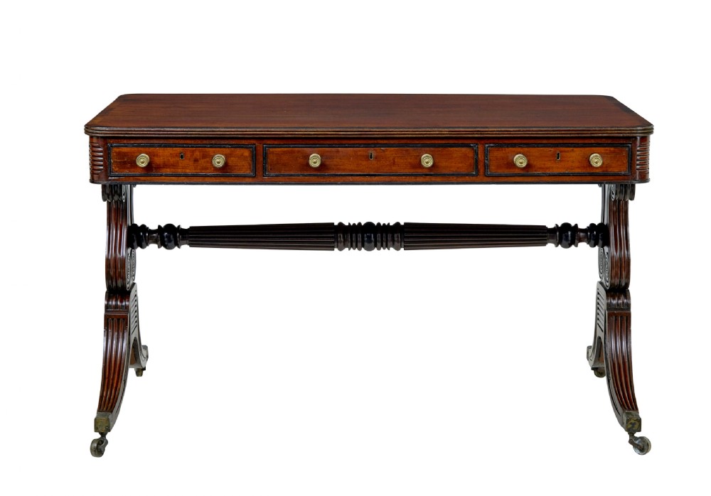 A 19th-century William IV mahogany library desk featuring three frieze drawers with brass knobs, carved scroll end supports, and a turned stretcher on brass castors. View III