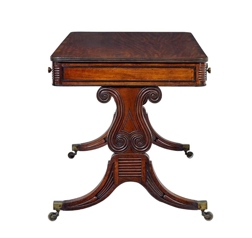 A 19th-century William IV mahogany library desk featuring three frieze drawers with brass knobs, carved scroll end supports, and a turned stretcher on brass castors. View VI