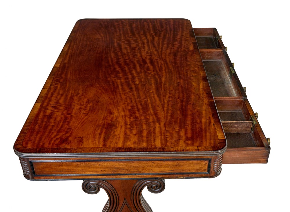 A 19th-century William IV mahogany library desk featuring three frieze drawers with brass knobs, carved scroll end supports, and a turned stretcher on brass castors. View VII
