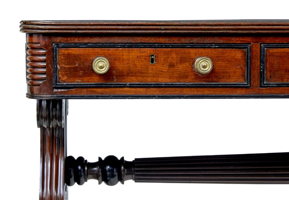 A 19th-century William IV mahogany library desk featuring three frieze drawers with brass knobs, carved scroll end supports, and a turned stretcher on brass castors. View XI