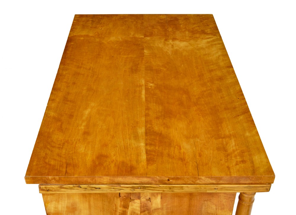 A 19th-century Swedish Empire satin birch chest of drawers featuring three drawers, flanking turned columns, an arched lower veneer panel, and angular block feet. View X
