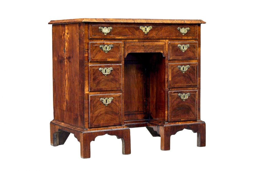 An eighteenth-century Queen Anne walnut kneehole desk featuring figured walnut veneers, brass drop handles, a central recessed cupboard, and bracket feet.