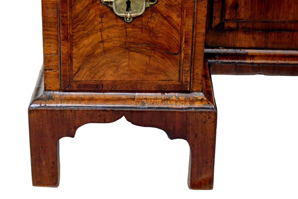 An eighteenth-century Queen Anne walnut kneehole desk featuring figured walnut veneers, brass drop handles, a central recessed cupboard, and bracket feet. View VII
