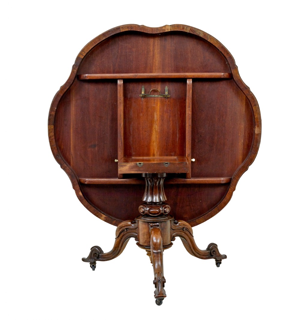 A 19th-century Victorian walnut centre table featuring intricate floral marquetry inlays, a shaped rim, and a carved central pedestal with four scroll legs on castors. View VI