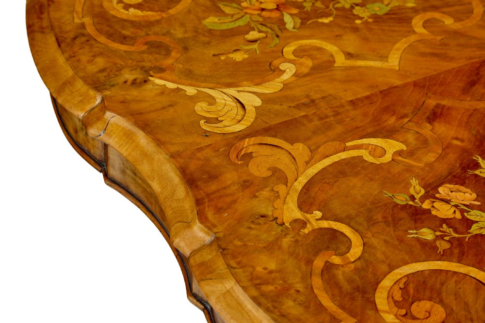 A 19th-century Victorian walnut centre table featuring intricate floral marquetry inlays, a shaped rim, and a carved central pedestal with four scroll legs on castors. View XV