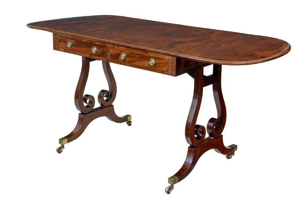 An early 19th-century mahogany sofa table featuring two drop leaves, twin frieze drawers with brass handles, and lyre-shaped scroll legs on brass castors. View II