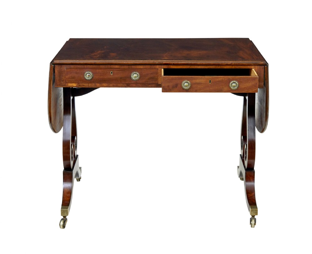 An early 19th-century mahogany sofa table featuring two drop leaves, twin frieze drawers with brass handles, and lyre-shaped scroll legs on brass castors. View IV