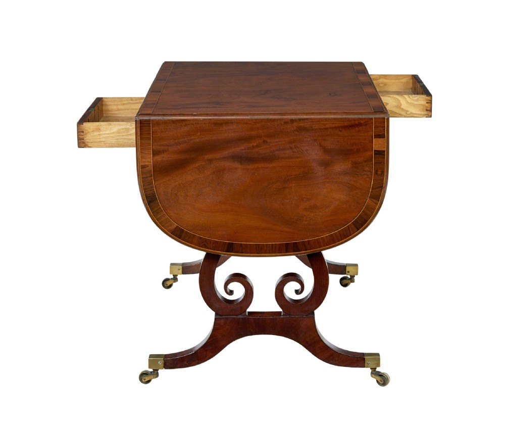 An early 19th-century mahogany sofa table featuring two drop leaves, twin frieze drawers with brass handles, and lyre-shaped scroll legs on brass castors. View V