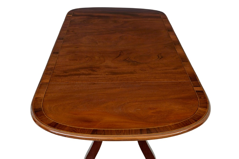 An early 19th-century mahogany sofa table featuring two drop leaves, twin frieze drawers with brass handles, and lyre-shaped scroll legs on brass castors. View IX