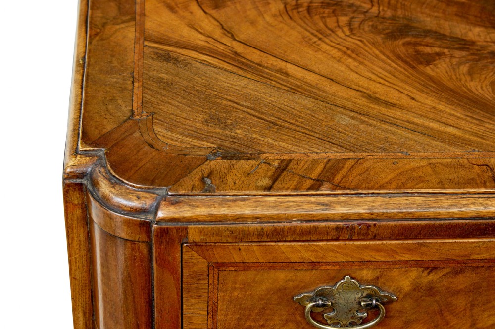 A four-drawer walnut chest featuring figured wood veneers, shaped bottom apron, brass handles, and rounded front corners. View V